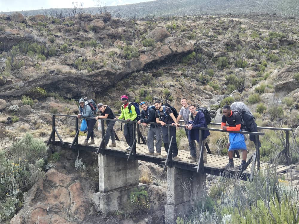 קבוצת מטיילים עם רייצ'ל חוצה גשר עץ מעל ערוץ טבעי
